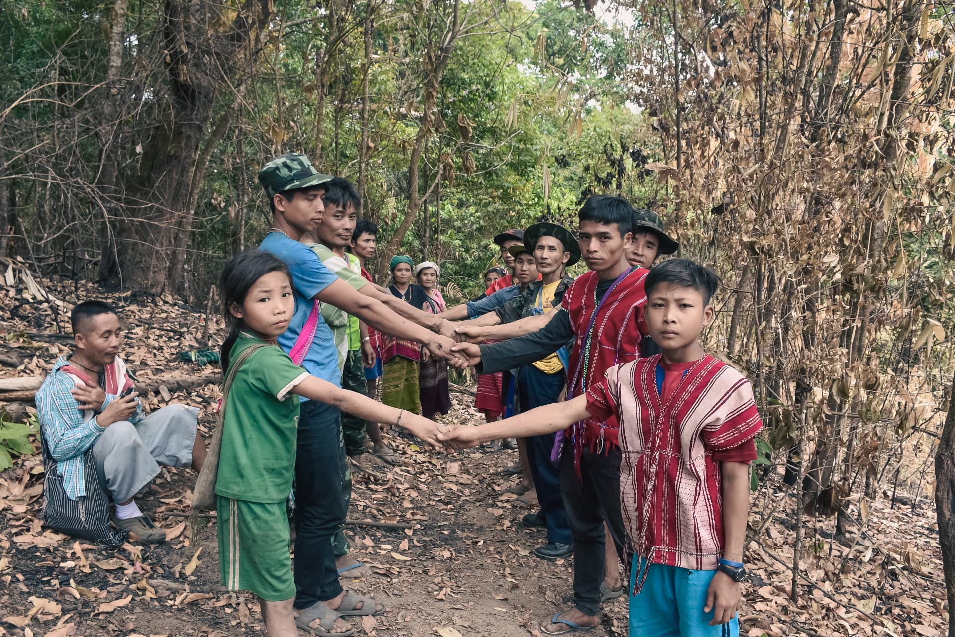 Community members of all ages joining hands along a forest path